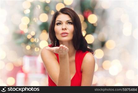 christmas, people, holidays and gesture concept - beautiful sexy woman in red dress sending blow kiss over holidays lights background