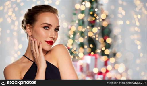 christmas, people, luxury and fashion concept - beautiful woman in black with red lips over holidays lights background