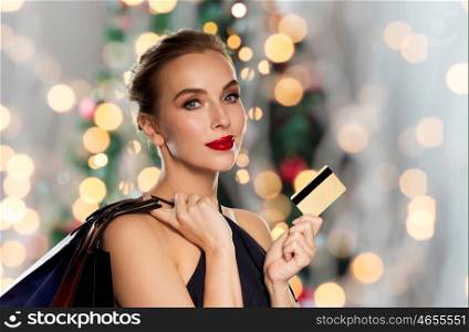 christmas, people, luxury and sale concept - beautiful woman with credit card and shopping bags over holidays lights background