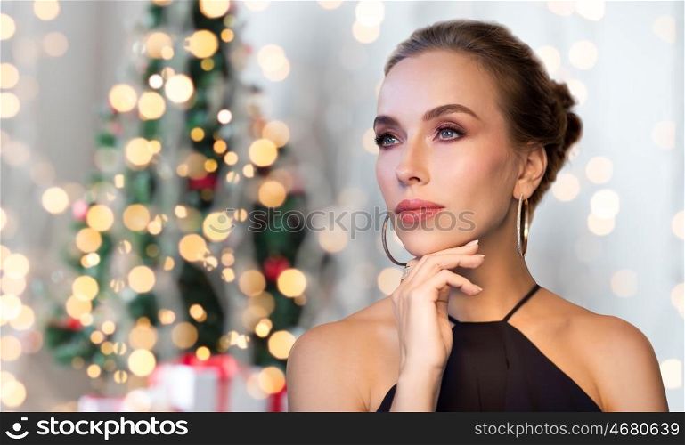 christmas, people, luxury, jewelry and fashion concept - beautiful woman in black wearing diamond earring and ring over holidays lights background