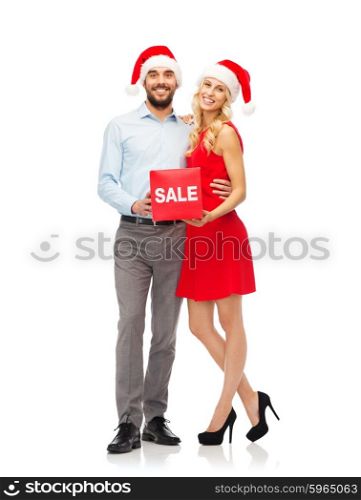 christmas, people, sale, discount and holidays concept - happy couple in santa hats with red sale sign