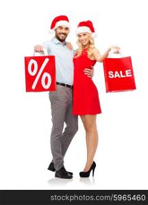 christmas, people, sale, discount and holidays concept - happy couple in santa hats hugging with red shopping bags