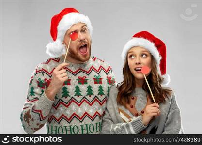 christmas, photo booth and holidays concept - happy couple in ugly sweaters posing with party props. couple with christmas party props in ugly sweaters