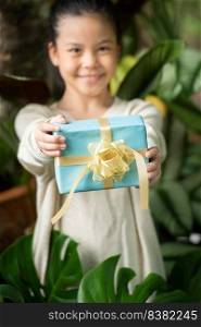 Christmas portrait of happy smiling little girl child with gift box near a green branch tree.