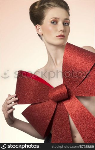 christmas portrait of sensual naked woman with elegant hair-style adorned with big red glitter bow, looking in camera