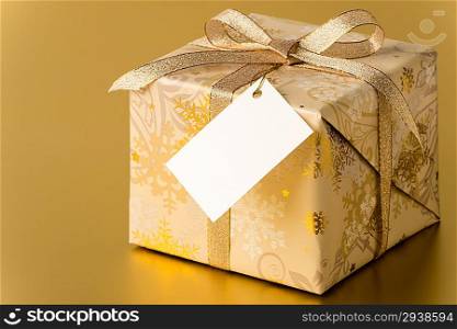 Christmas present with ribbon and blank tag on gold background copyspace