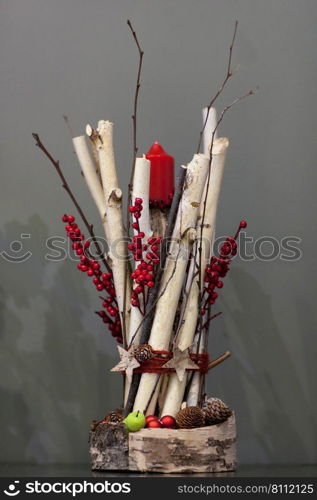 Christmas red candle decorated with a bunch of wooden twigs and berries and fir cones on a gray background. Decorations Christmas candles on gray background