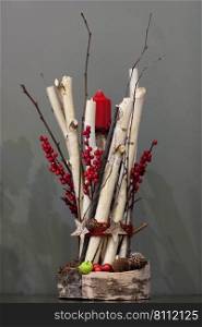 Christmas red candle decorated with a bunch of wooden twigs and berries and fir cones on a gray background. Decorations Christmas candles on gray background