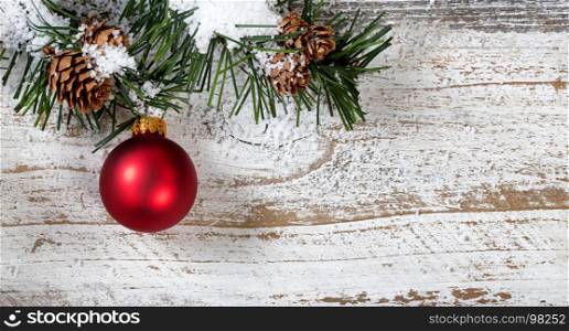 Christmas red ornament hanging in rough fir tree branch on rustic white wooden background