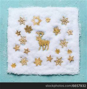 Christmas reindeer in snow with golden snowflakes on light blue background, top view. Flat lay. Winter composition and holiday concept