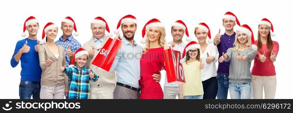 christmas sale and holidays concept - group of happy people in santa hats with shopping bags showing thumbs up. people in santa hats with sale sign at christmas