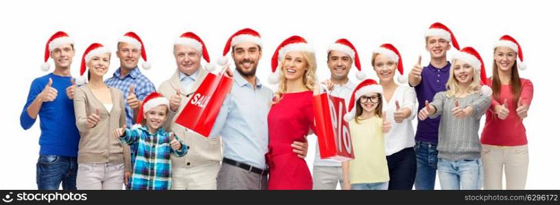 christmas sale and holidays concept - group of happy people in santa hats with shopping bags showing thumbs up. people in santa hats with sale sign at christmas