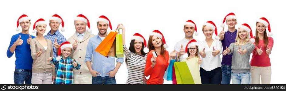 christmas sale and holidays concept - group of people in santa hats with shopping bags showing thumbs up. people with shopping bags at christmas sale