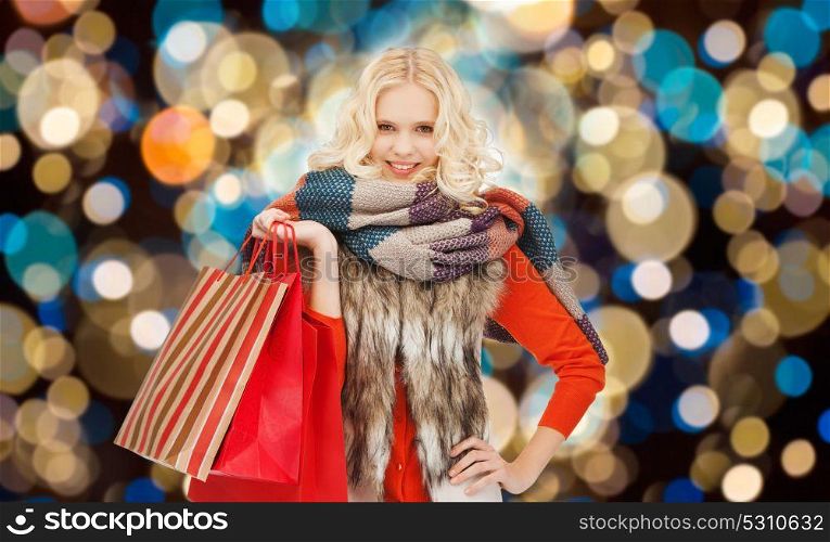 christmas sale and people concept - happy teenage girl or young woman in winter clothes with shopping bags over holidays lights background. young woman in winter clothes with shopping bags
