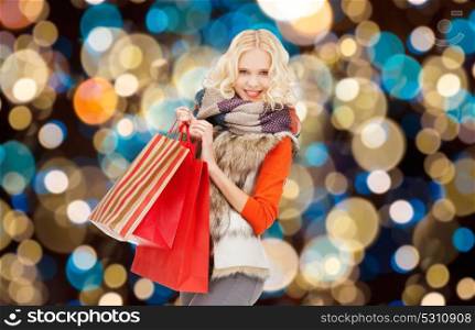 christmas sale and people concept - happy teenage girl or young woman in winter clothes with shopping bags over holidays lights background. young woman in winter clothes with shopping bags