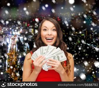 christmas, sale, banking, winning and holidays concept - smiling woman in red dress with us dollar money over snowy night city background