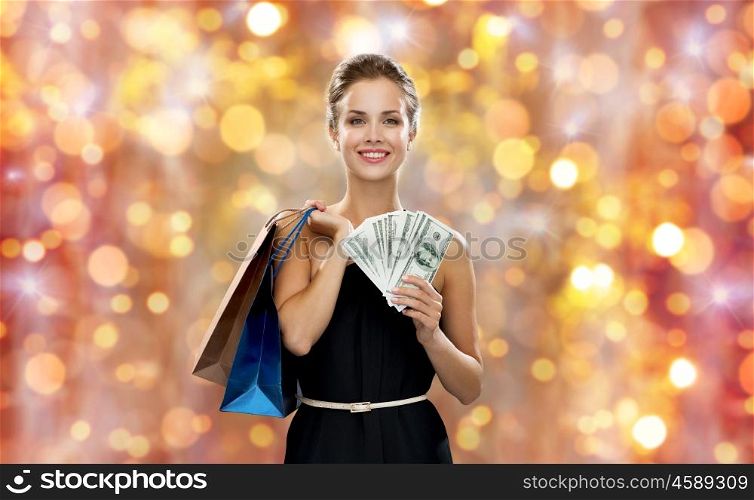 christmas, sale, people, money and holidays concept - smiling woman in dress with shopping bags and money over lights background