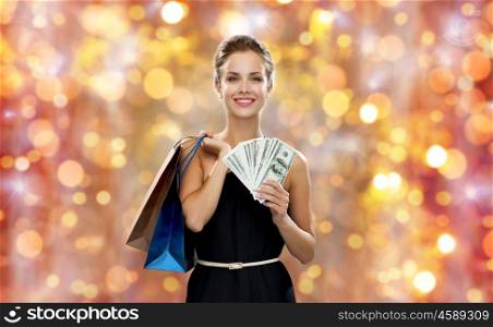 christmas, sale, people, money and holidays concept - smiling woman in dress with shopping bags and money over lights background