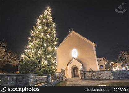 Christmas scenery in Ehrwald, Austria, at night. Christmas tree and church and Xmas lights. Outdoor Christmas decor in the Austrian village.