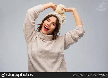 christmas, season and clothes concept - happy smiling young woman in knitted winter hat and sweater over grey background. young woman in knitted winter hat and sweater