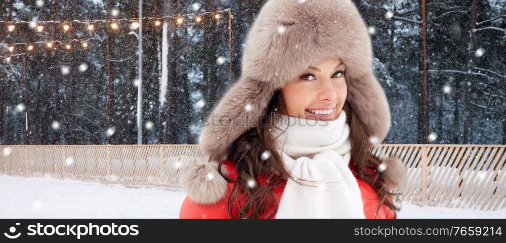 christmas, season and holidays concept - close up of happy woman in winter fur hat over outdoor ice skating rink on background. smiling woman in winter hat over ice skating rink