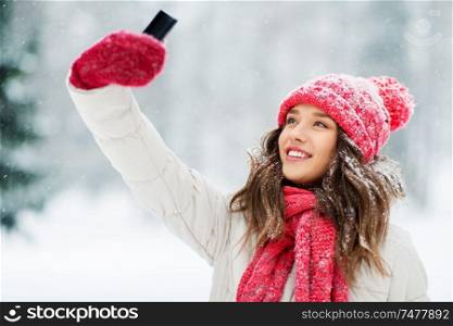 christmas, season and people concept - happy smiling teenage girl or young woman taking selfie by smartphone in winter park. young woman taking selfie by smartphone in winter