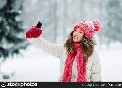 christmas, season and people concept - happy smiling teenage girl or young woman taking selfie by smartphone in winter park. young woman taking selfie by smartphone in winter