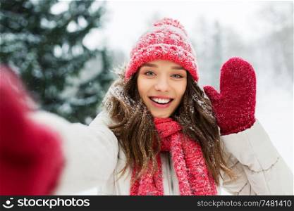 christmas, season and people concept - happy smiling woman taking selfie and waving hand outdoors in winter park. smiling woman taking selfie outdoors in winter
