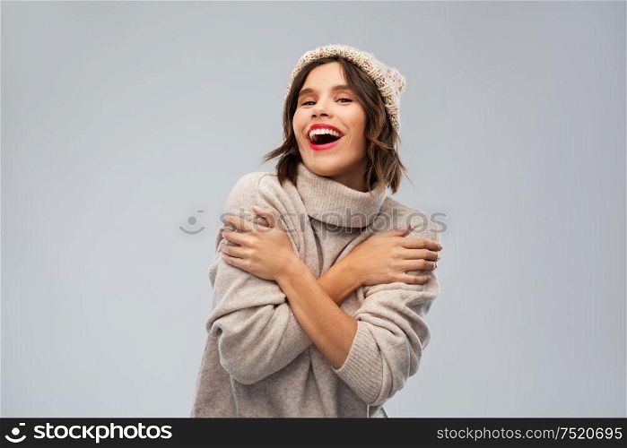 christmas, season and people concept - happy smiling young woman in knitted winter hat and sweater over grey background. young woman in knitted winter hat and sweater