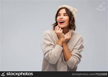christmas, season and people concept - happy smiling young woman in knitted winter hat and sweater over grey background. young woman in knitted winter hat and sweater