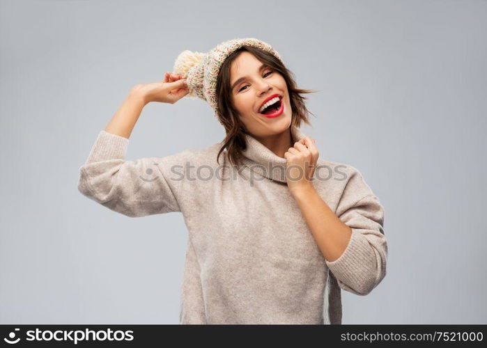 christmas, season and people concept - happy smiling young woman in knitted winter hat and sweater over grey background. young woman in knitted winter hat and sweater