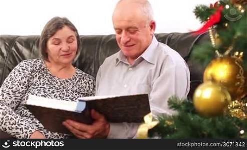 Christmas - senior couple going through photo album at Holiday time. They are out focus and then comes in focus when camera far away from them.