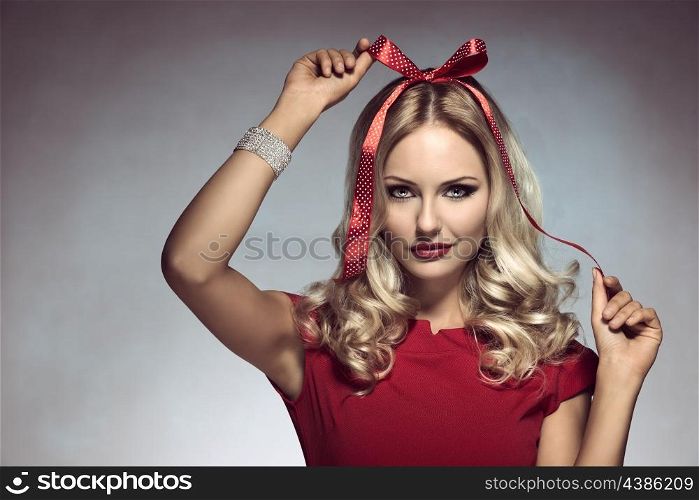 christmas shoot of funny blonde girl with pois bow on her head, adorned like a xmas gift, wearing elegant red dress and bracelet