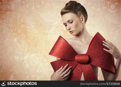 christmas shoot of sensual young girl adorned like a present with elegant hair-style, colorful make-up and big red glitter bow on her beast,