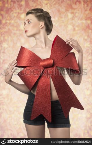 christmas shoot of sensual young girl with elegant hair-style, colorful make-up and big red bow on her beast, adorned like a present