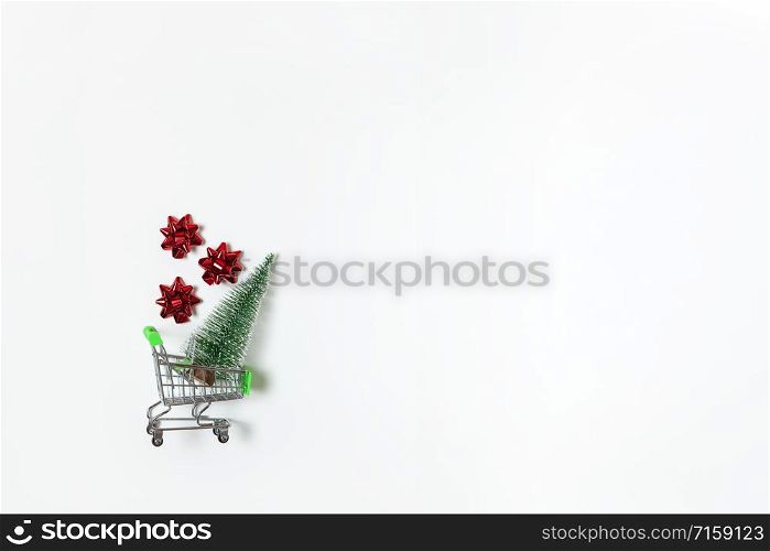 Christmas snow covered fir and red bows for gift in toy shopping cart on white background, copy space. New Year, sales, online shopping concept. Horizontal, flat lay. Minimal style. Top view.