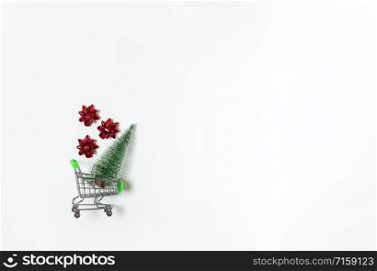 Christmas snow covered fir and red bows for gift in toy shopping cart on white background, copy space. New Year, sales, online shopping concept. Horizontal, flat lay. Minimal style. Top view.