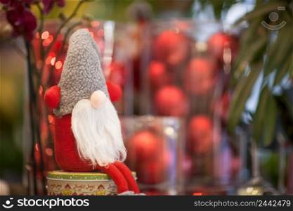 Christmas soft toy Santa Claus on a box with a gift on a background of red balls. soft Christmas toys and decorations
