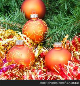 Christmas still life - several orange and yellow Christmas baubles, red tinsel on green Xmas tree background