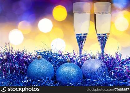 Christmas still life - two glasses of champagne and blue Xmas balls with yellow and violet blurred Christmas lights bokeh background