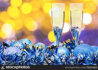 Christmas still life - two glasses of champagne at blue Xmas decorations with yellow and violet blurred Christmas lights background