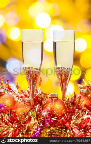 Christmas still life - two glasses of champagne at red and golden Xmas decorations with yellow and violet blurred Christmas lights bokeh background