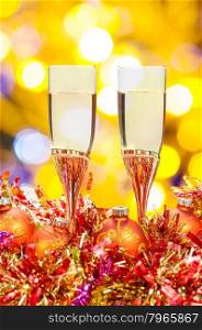 Christmas still life - two glasses of champagne at red and golden Xmas decorations with yellow and violet blurred Christmas lights bokeh background