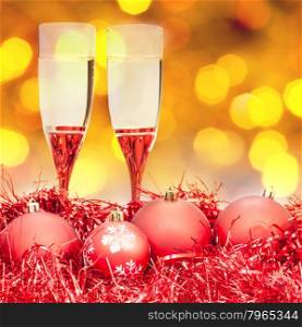 Christmas still life - two glasses of champagne at red Xmas decorations with yellow and violet blurred Christmas lights bokeh background