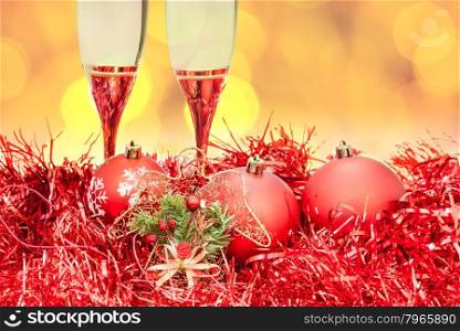 Christmas still life - two glasses of champagne at red Xmas decorations with yellow and violet blurred Christmas lights bokeh background