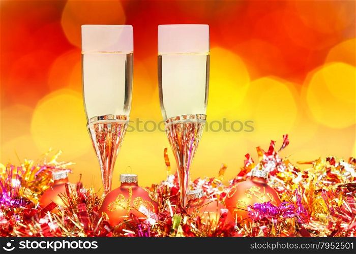 Christmas still life - two glasses of sparkling wine at golden Xmas decorations with red and yellow blurred Christmas lights background