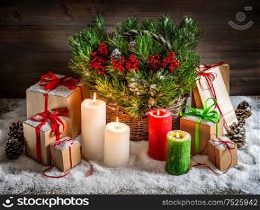 Christmas still life with burning candles and gift box. Christmas tree branches in basket. Vintage style toned picture with light effects