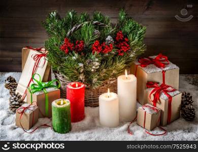 Christmas still life with burning candles and gift box. Christmas tree branches in basket. Vintage style toned picture with light effects