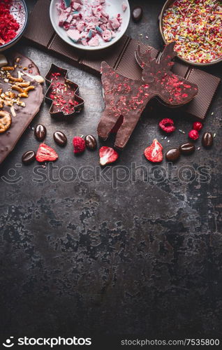 Christmas sweet gifts. Various chocolate in shape of Christmas symbols: Christmas tree, deer on dark background with copy space. Top view. Chocolate bark with topping