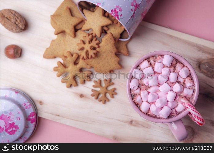 Christmas sweets context with a cup of hot cocoa with pink mini marshmallows, an overturned box with gingerbread cookies on a wooden platter.